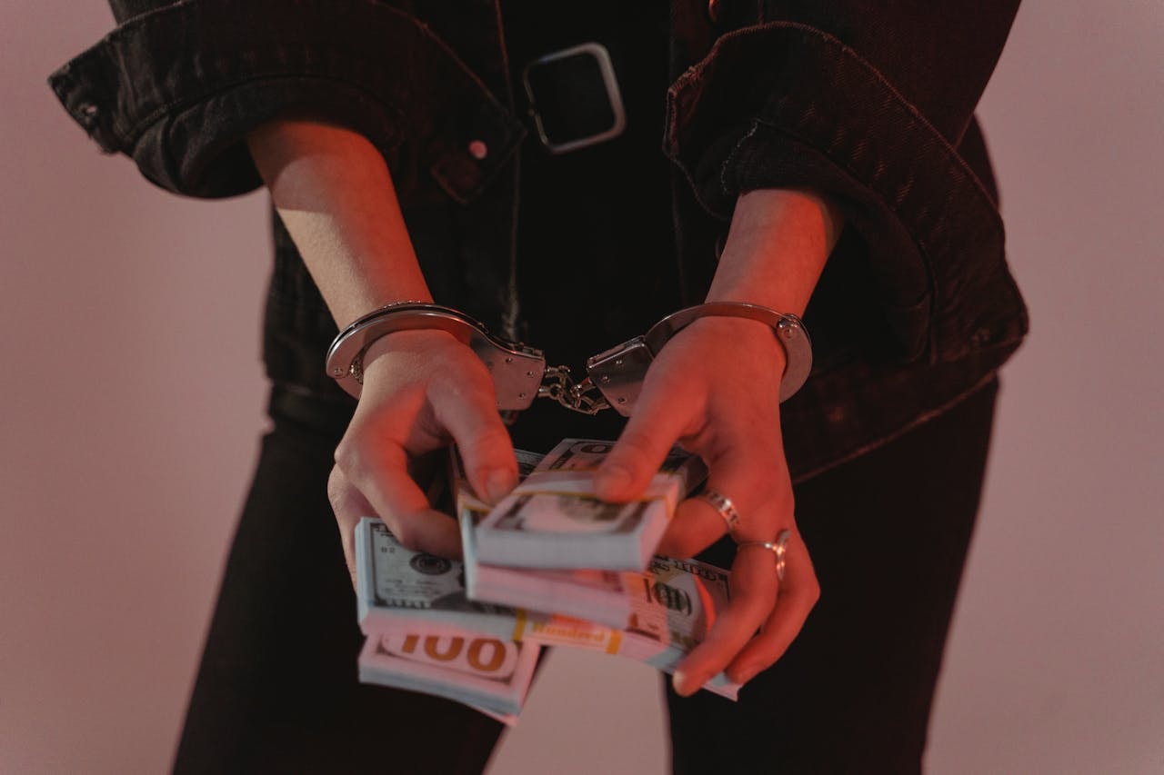 A handcuffed person holding paper bills