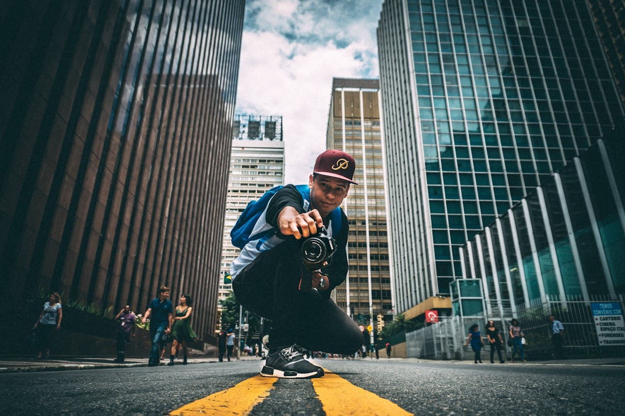 A man holding a camera in a city street surrounded by tall buildings