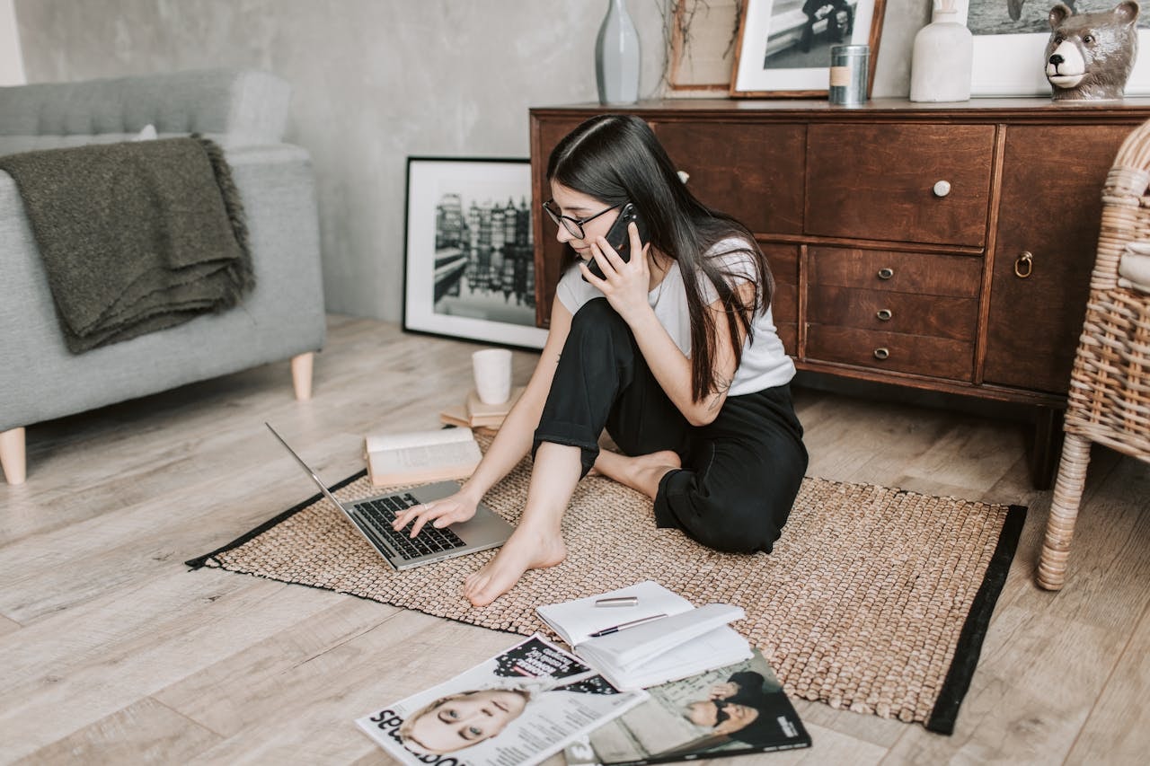 A woman sitting on the floor and talking on the phone while typing on a laptop