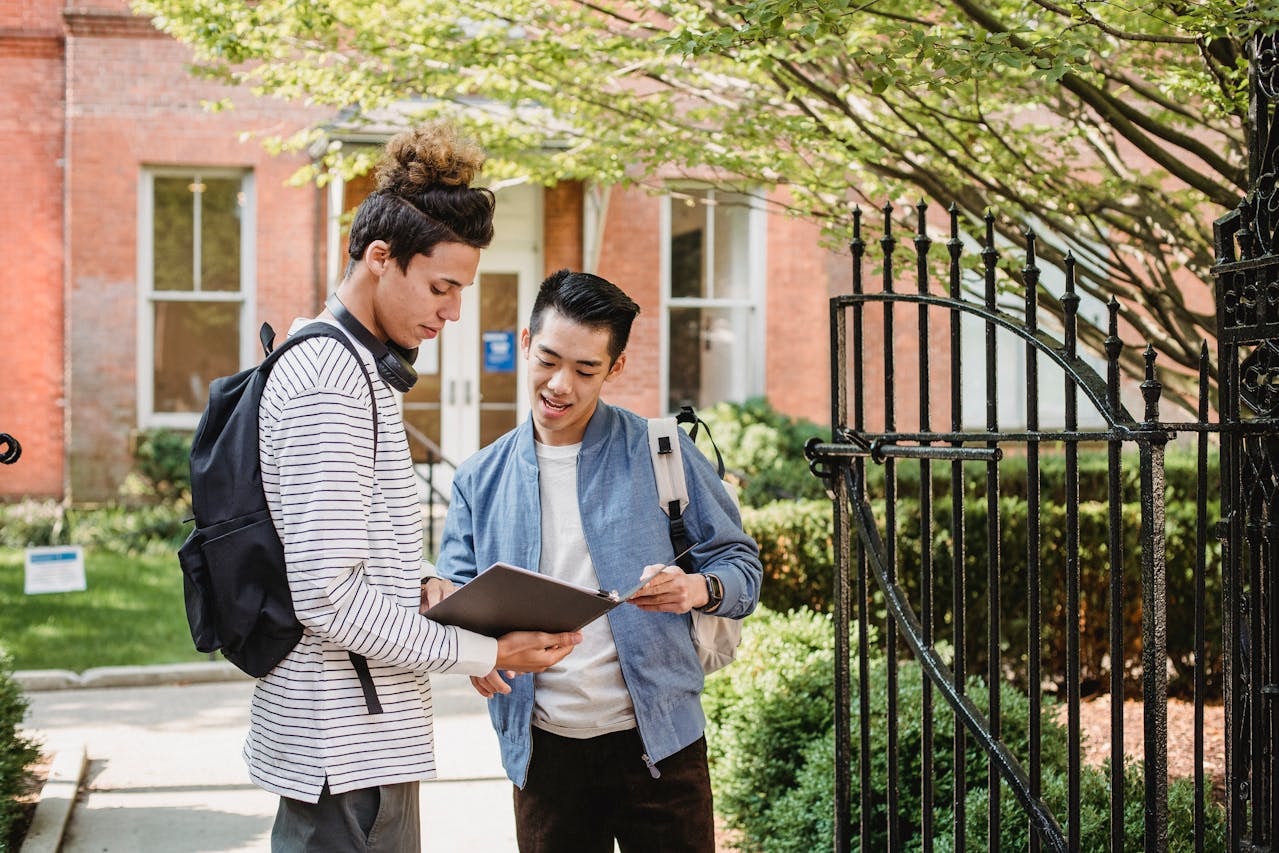 Two male students standing in front of a gate reading a document