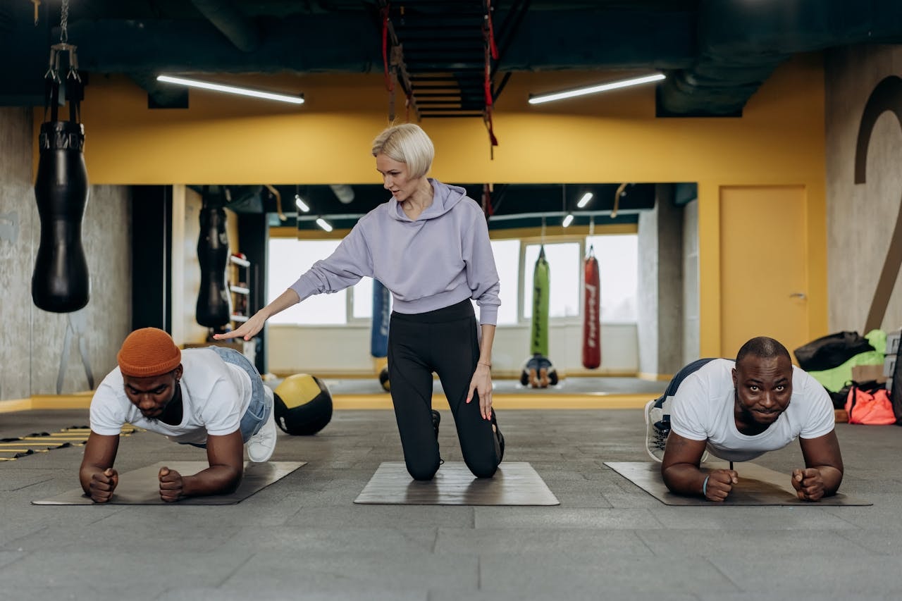 Two men doing push ups and being guided by a female fitness center attendant