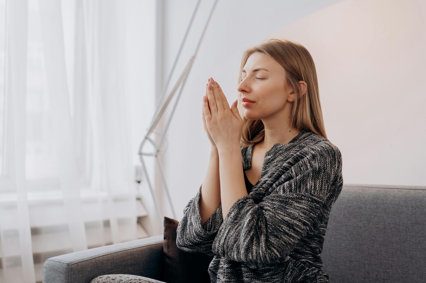 Woman in Black Long Sleeve Shirt Sitting on Gray Couch Praying.