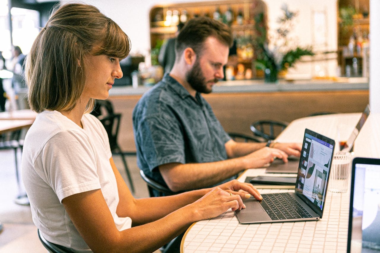 A man and a woman sitting next to each other and using laptops