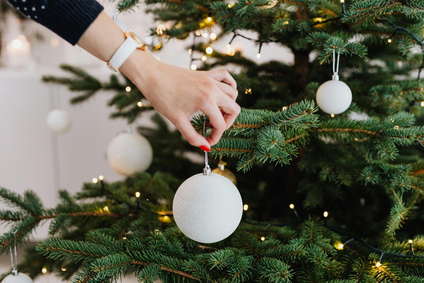 A person decorating a Christmas tree with ornaments.