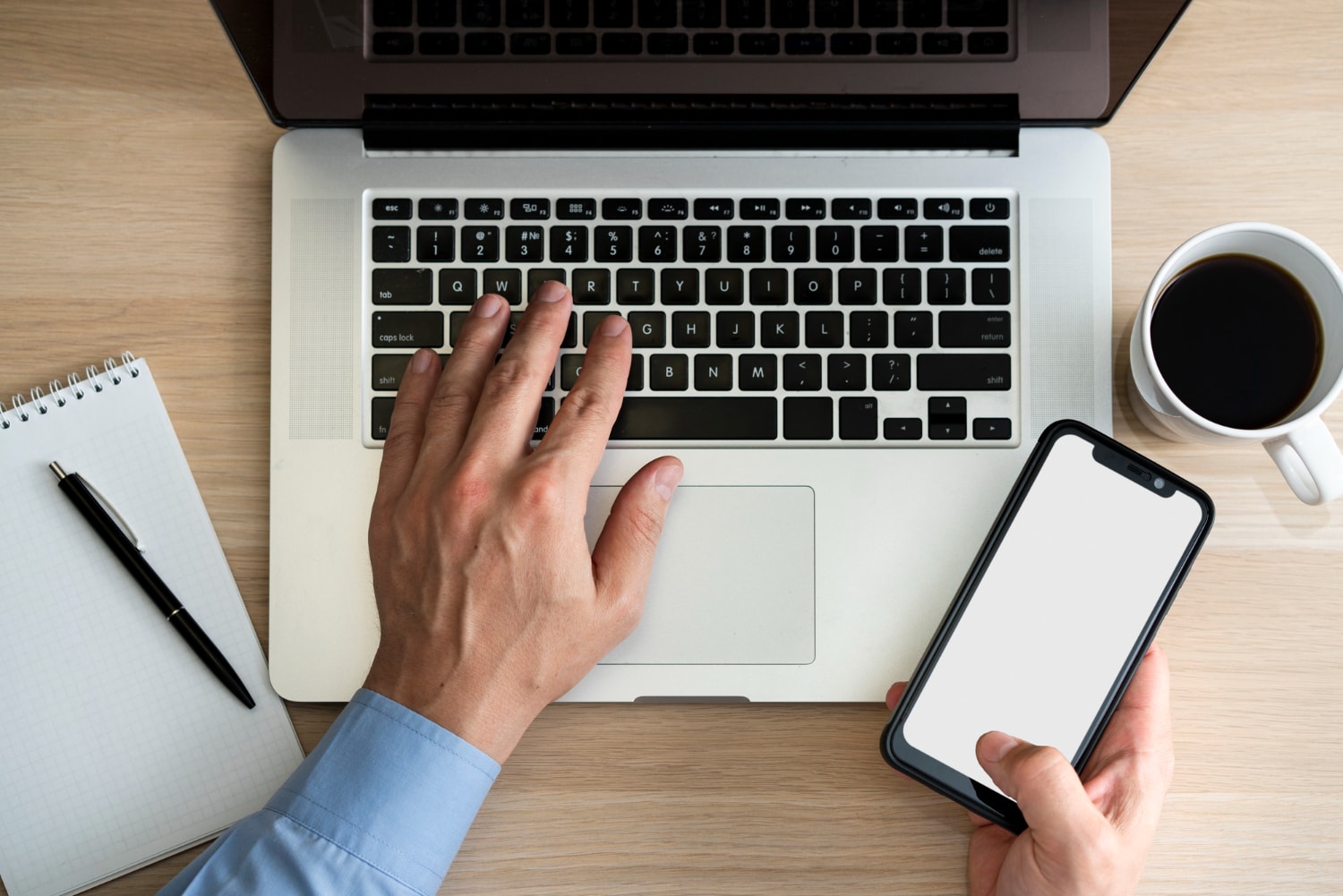 A person holding a cell phone and looking at a laptop appears ready to be responsive