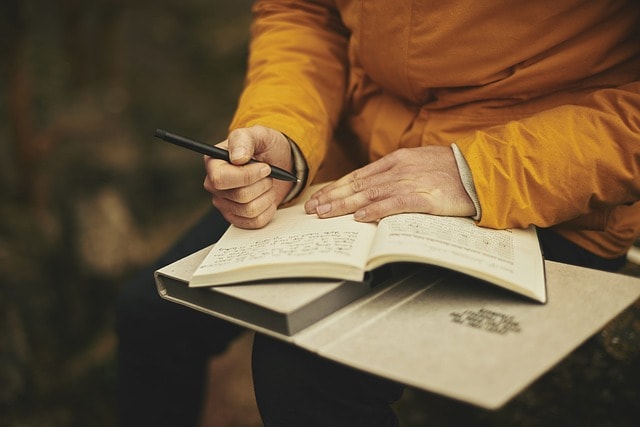 A person jotting down notes in a notebook resting on their lap.