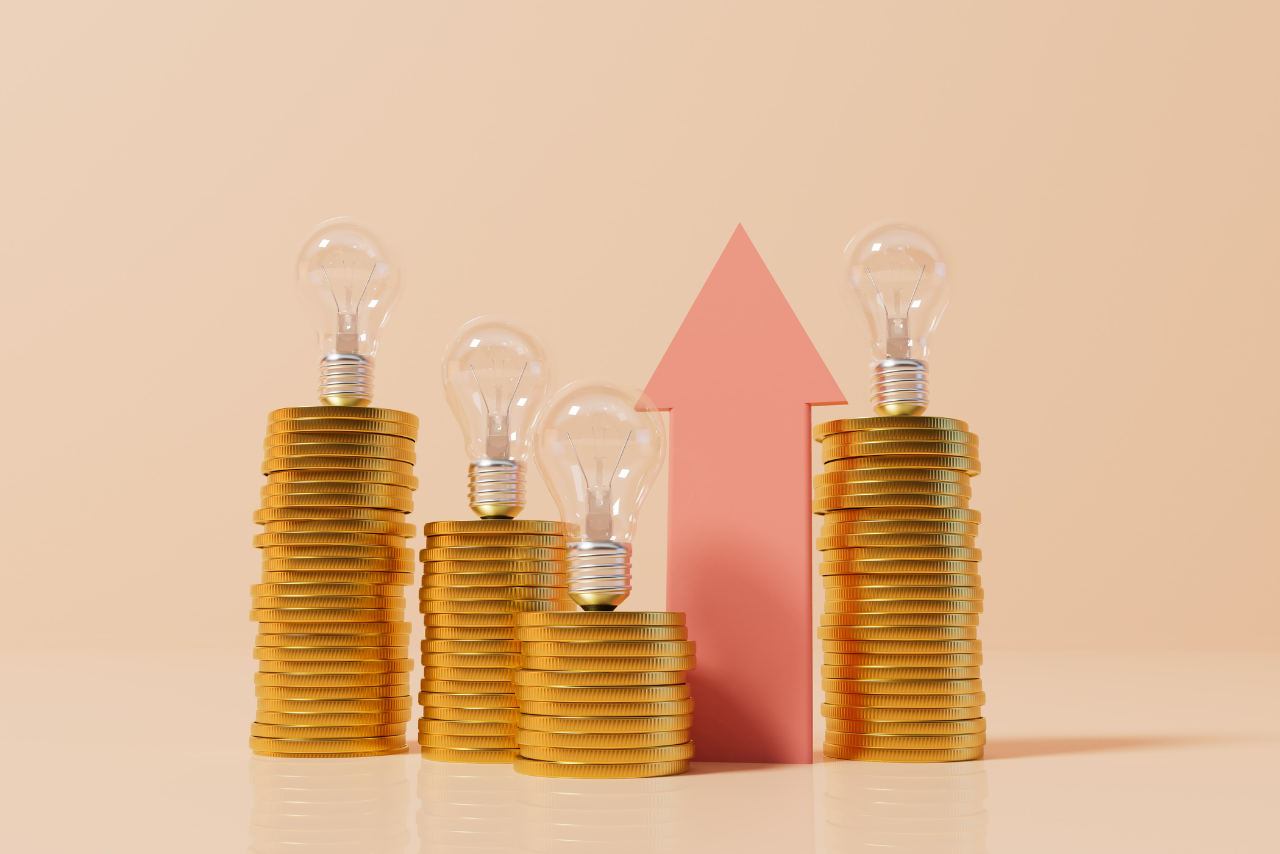 An image depicting stacked coins, a lightbulb, and an upward-pointing arrow, symbolizing a rise in prices.
