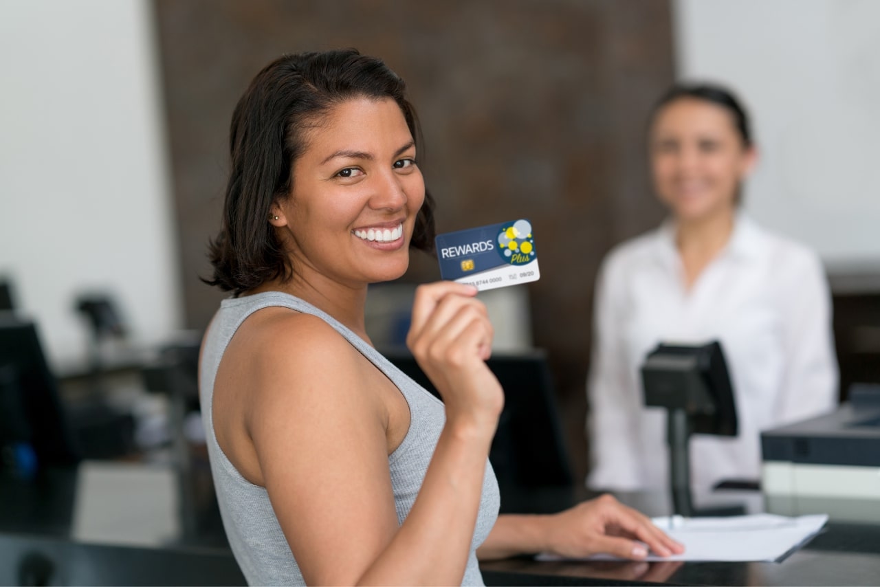 Beautiful woman on checking out and holding a loyalty rewards card looking at camera smiling.