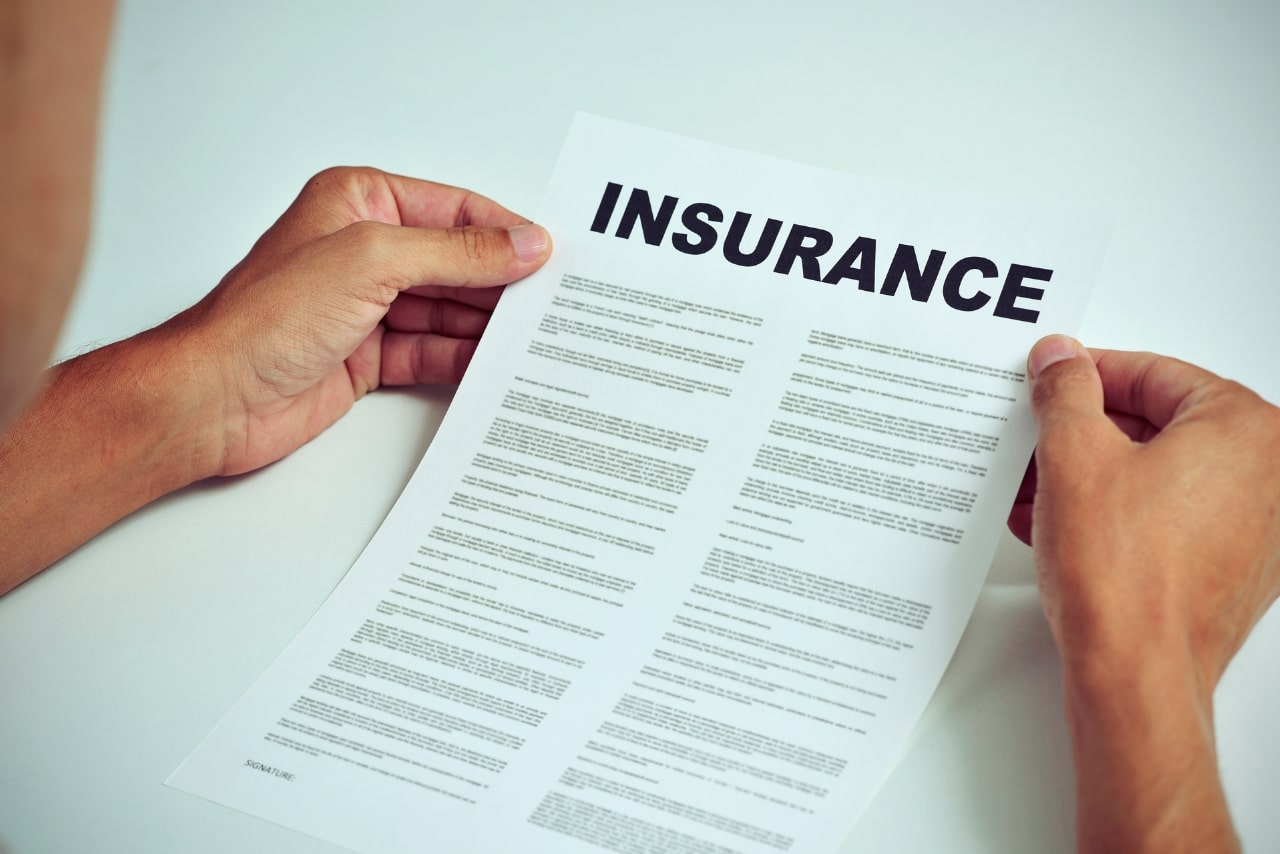 Closeup of young man sitting at a white table reading terms of insurance paper.