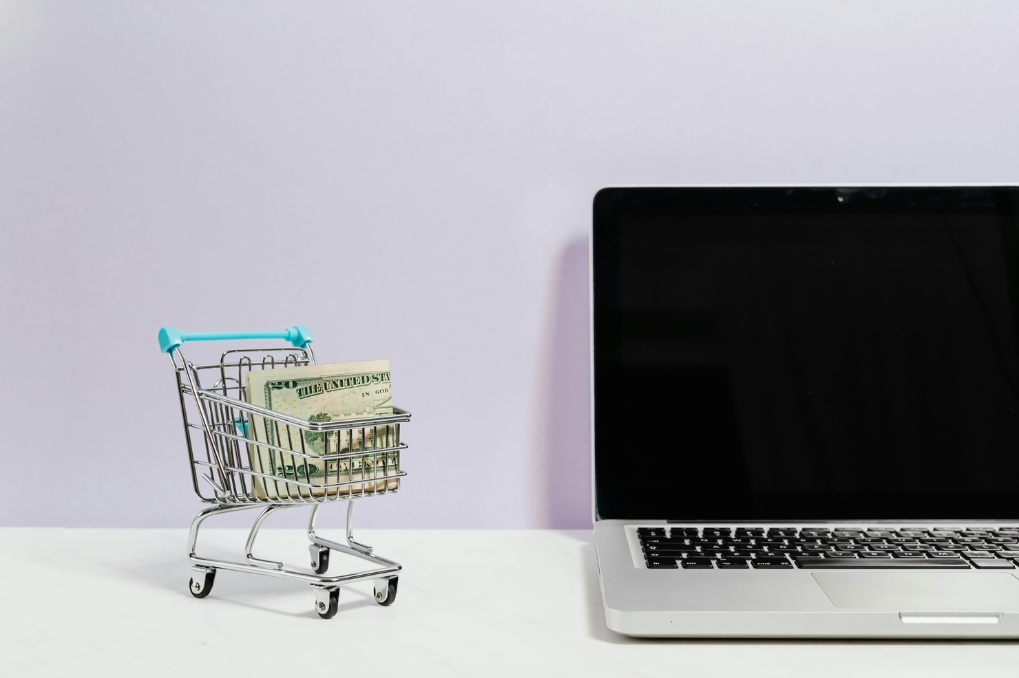Laptop computer, shopping trolley and dollars on table.