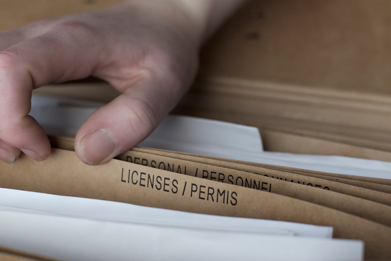 Man scanning a pile of folders with Licenses/Permis written on it.