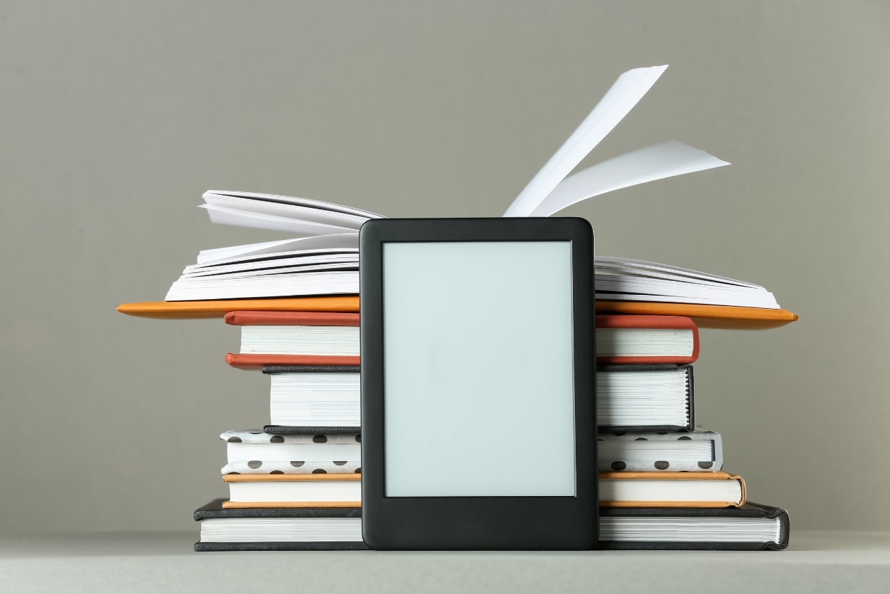 Modern E-Book Reader and Stack of Hard Cover Books on Light Grey.