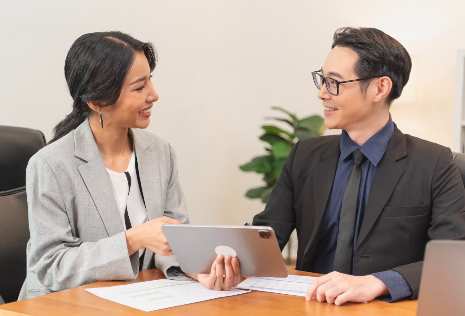 Smiling asian business woman showing tablet to her client.