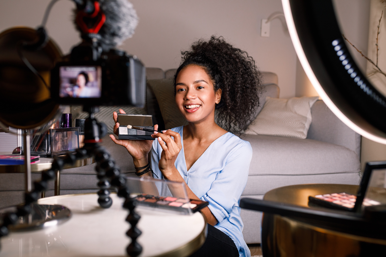 Smiling woman while holding makeup and recording herself.