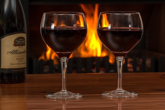 Two goblet glasses with red wine inside and bottle beside it.