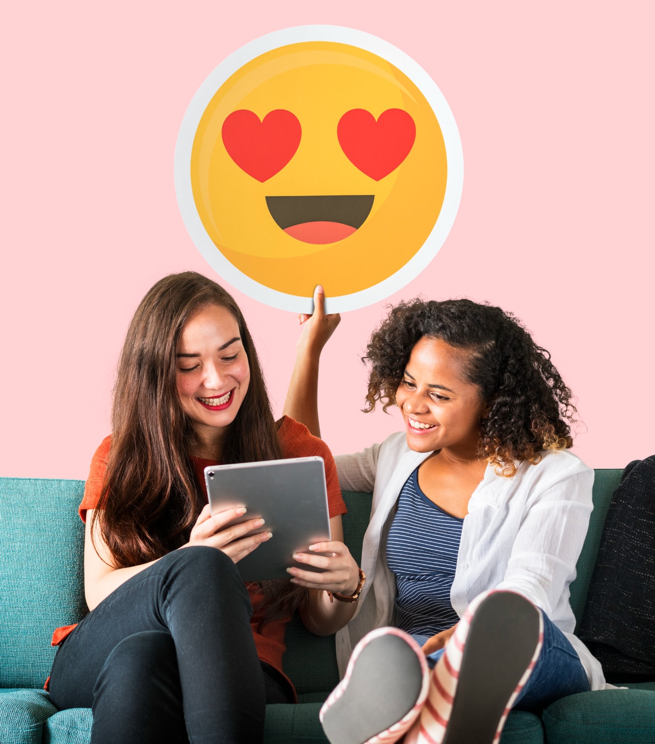 Women holding a heart eyes emoticon and using a tablet.