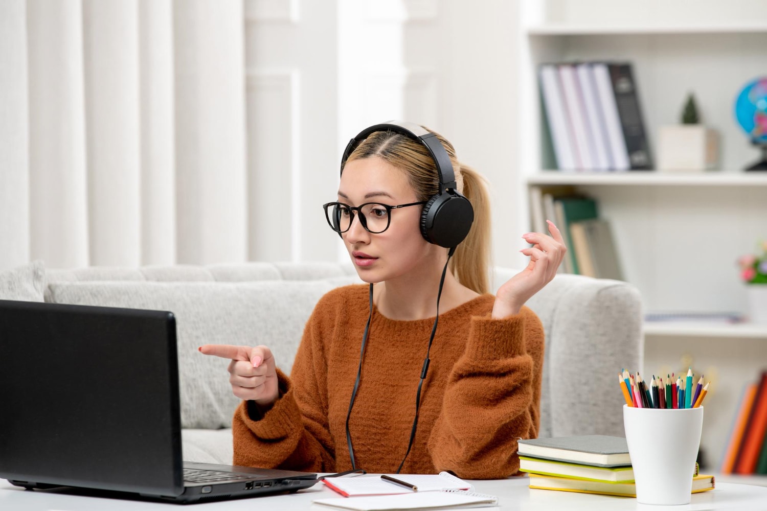 Young cute girl with glasses and orange sweater studying on computer.
