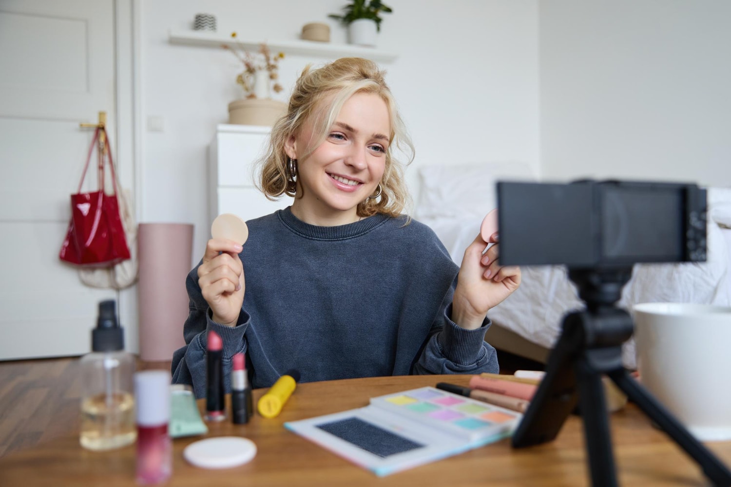 Young woman beauty content creator sitting in a room in front of digital camera.