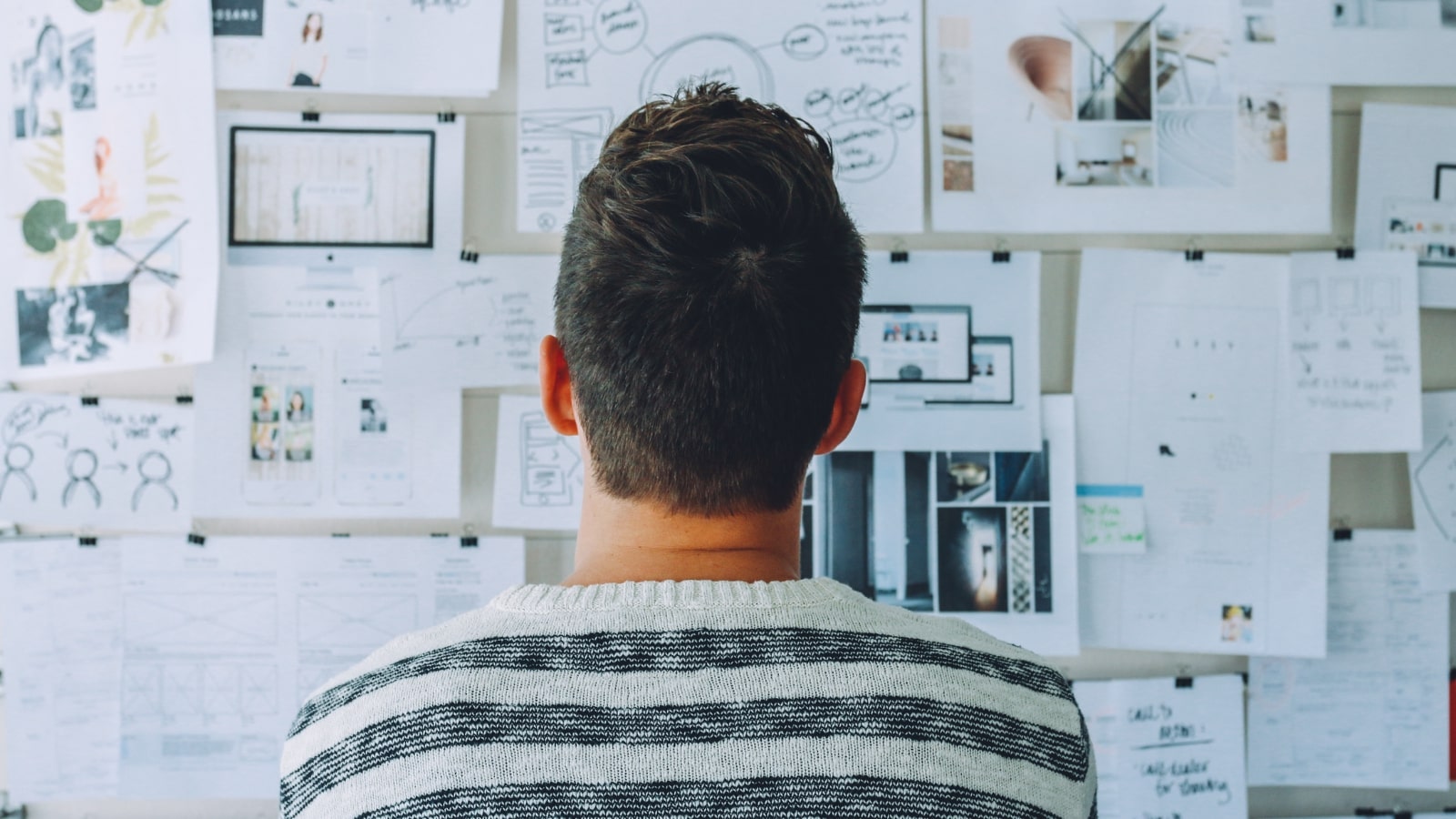 A back view of a man examining papers on a board while strategizing for his business.