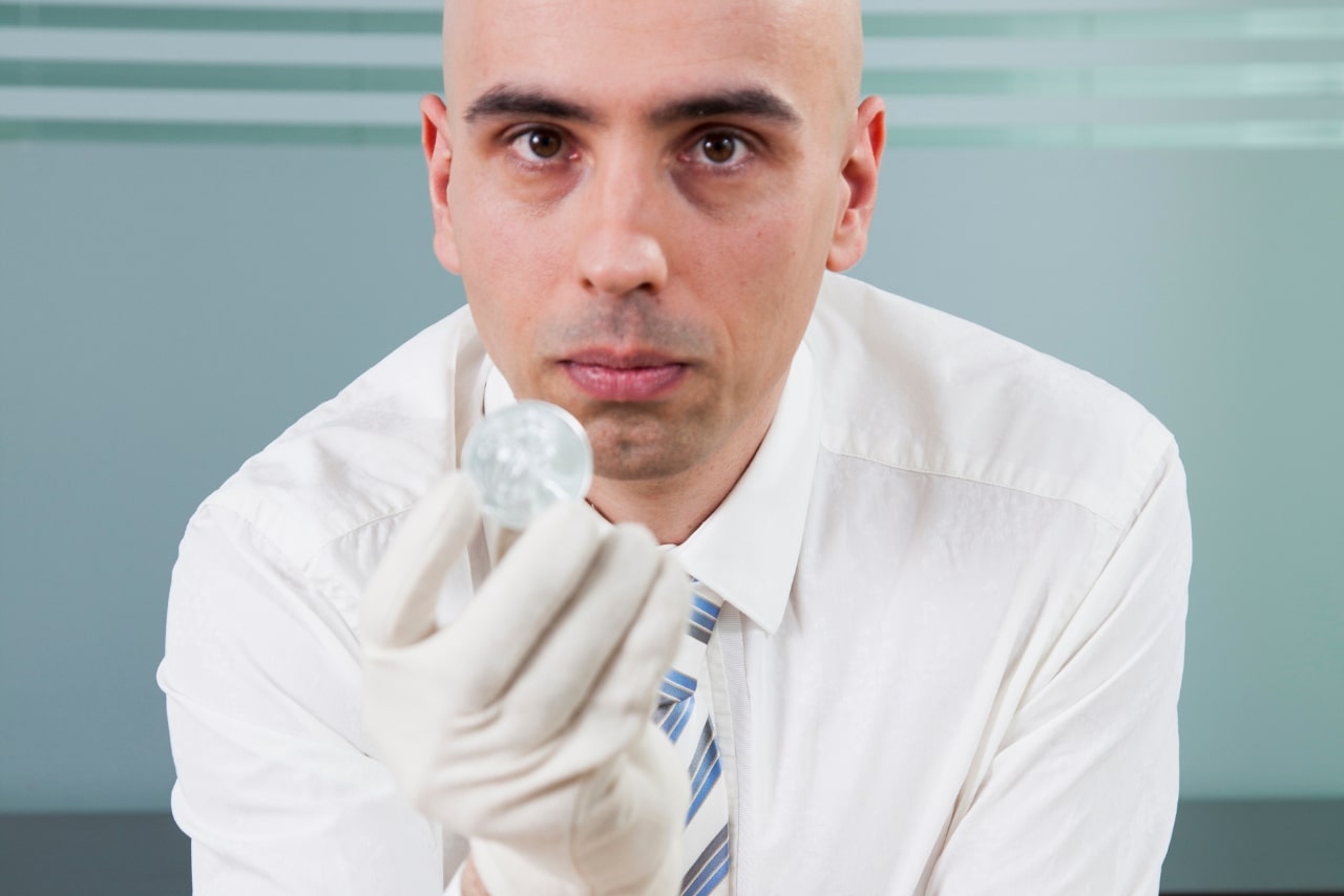 A bald man holds a silver coin.