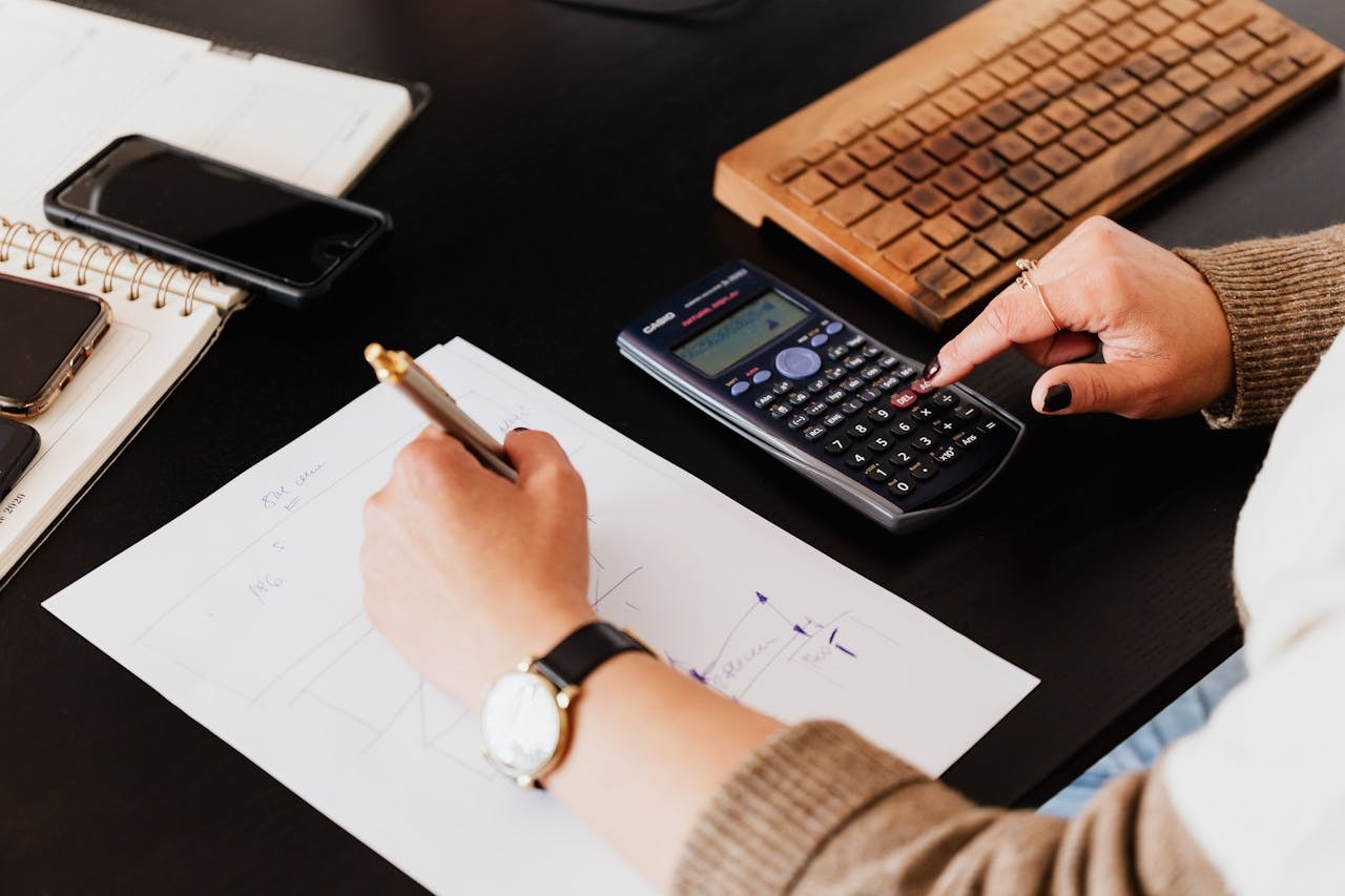 A bookkeeper using a calculator while writing on a white piece of paper