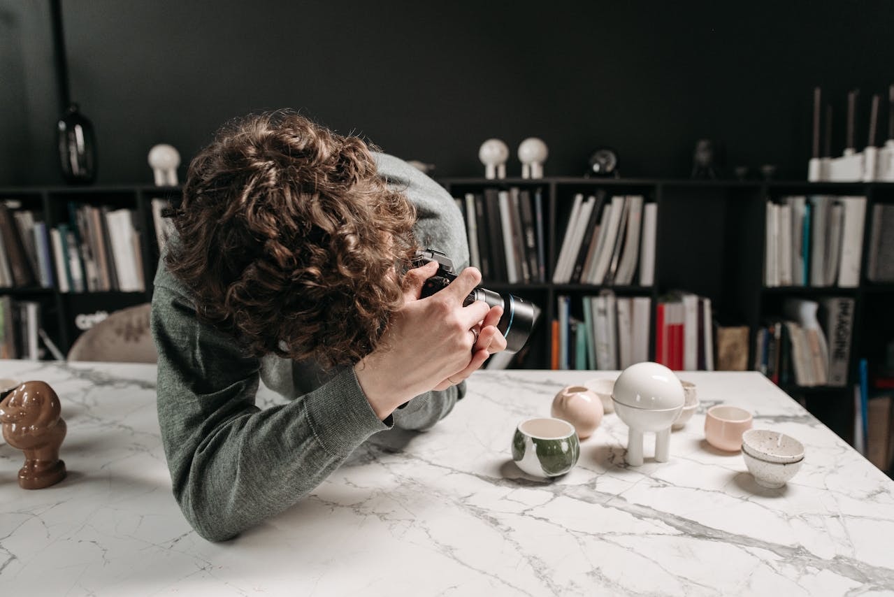 A man taking a picture of small ceramic products placed at the edge of a table