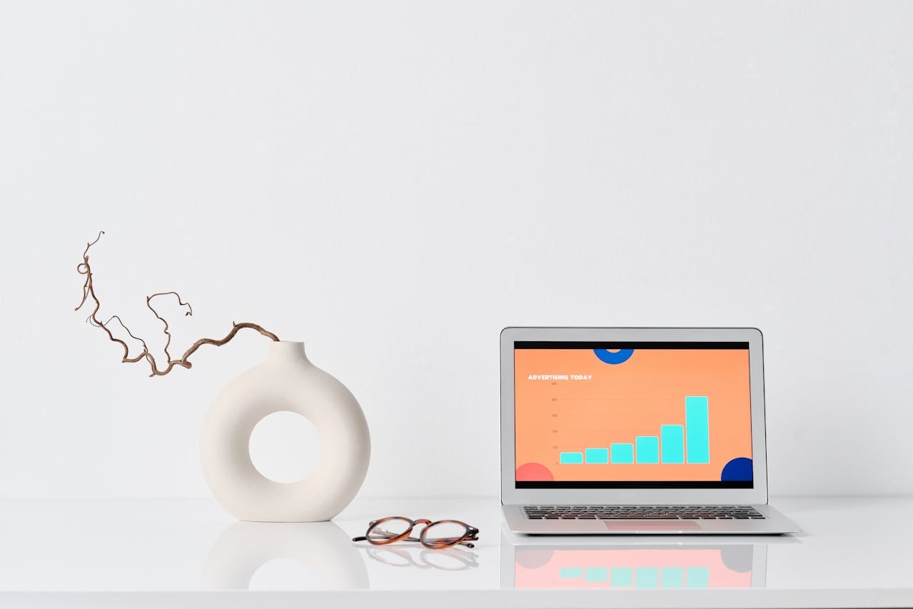 A photo of a laptop next to a vase and eyeglasses on a table
