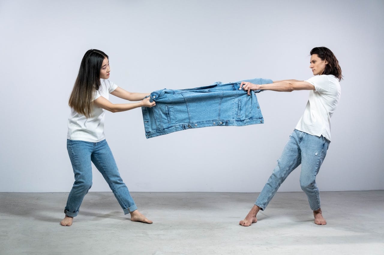 A photo of a man and a woman model holding one denim jacket on opposite ends