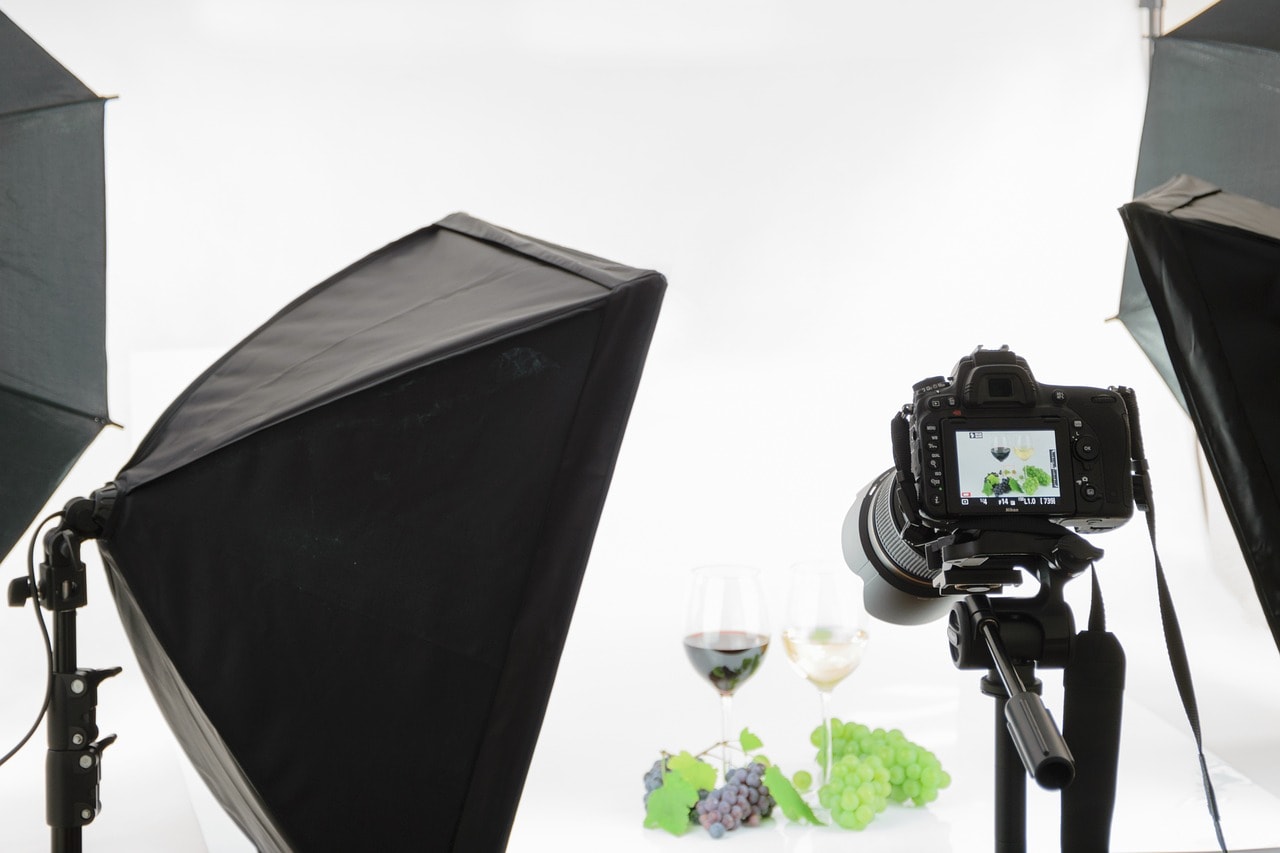 A photoshoot setup of red and white wine showing a camera attached to a tripod, reflectors, and white backdrop