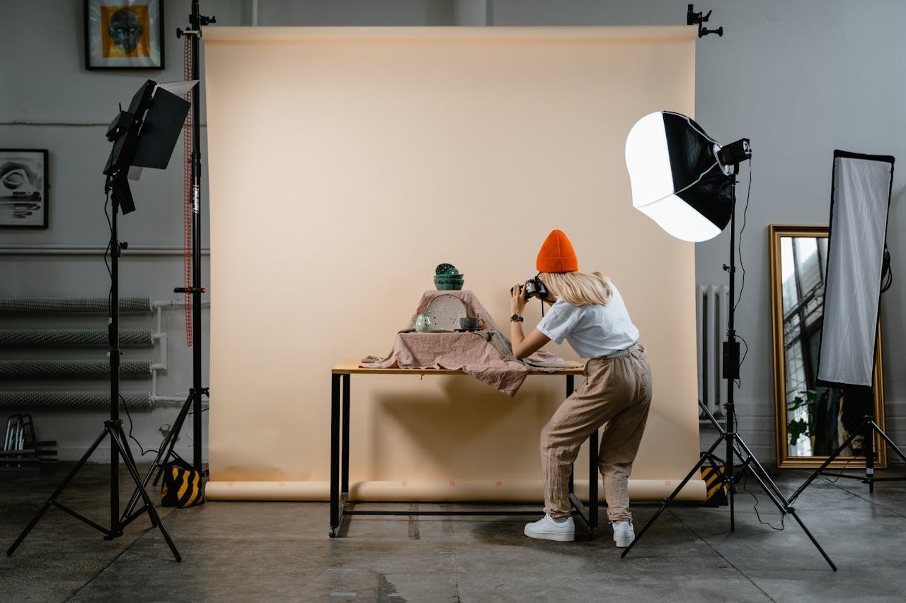A woman taking pictures of ceramic products on a table with lighting and white backdrop