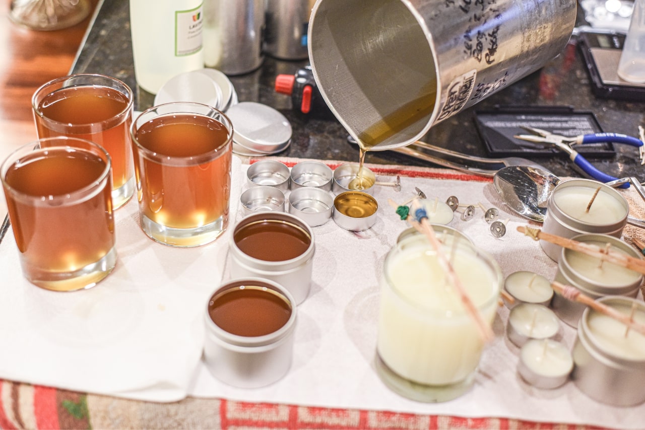Candle making showing the pouring of liquid wax into jars.