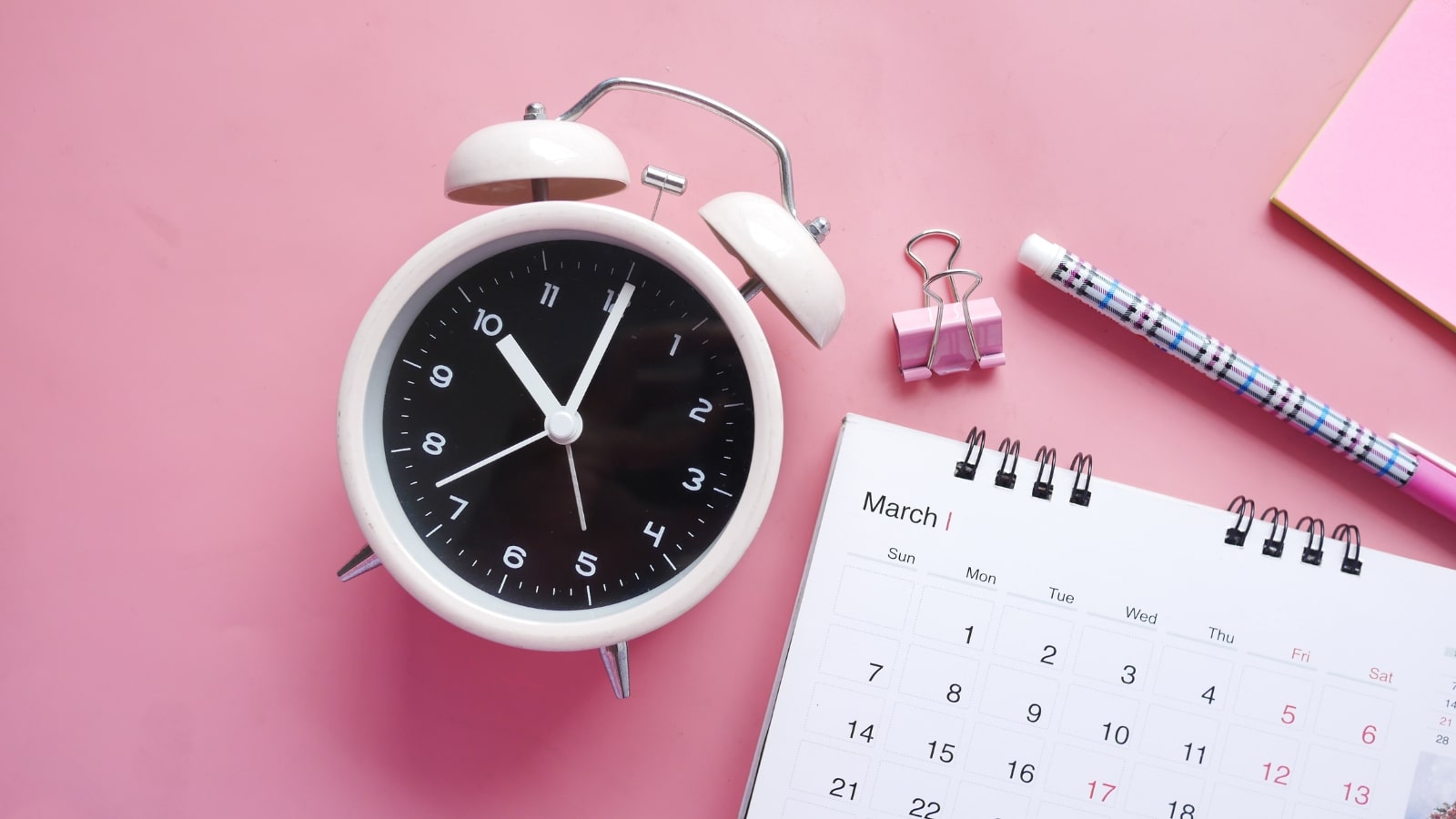 Close-up shot of an alarm clock and a calendar signifying regularity.