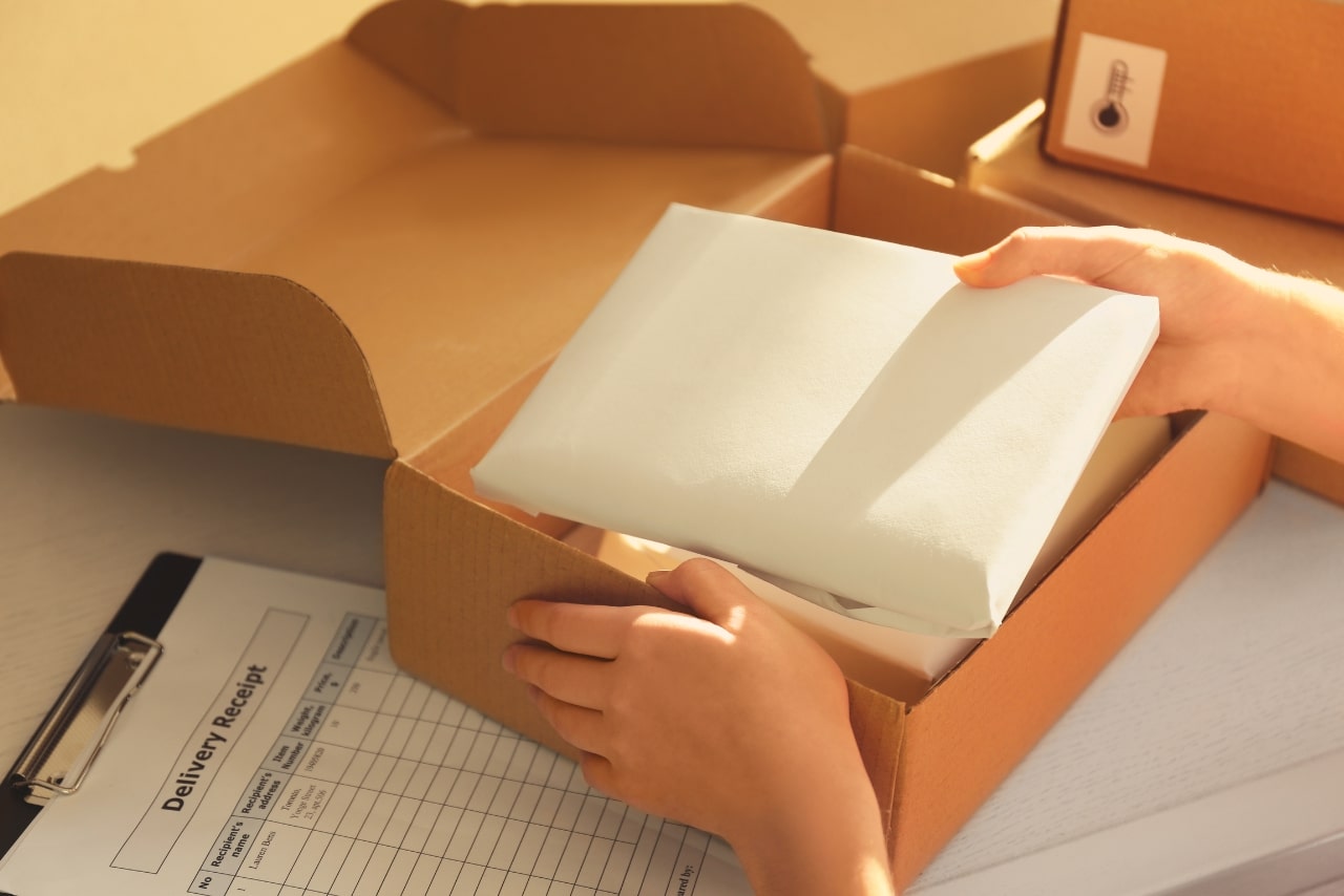 Courier hands are packaging parcel at table.