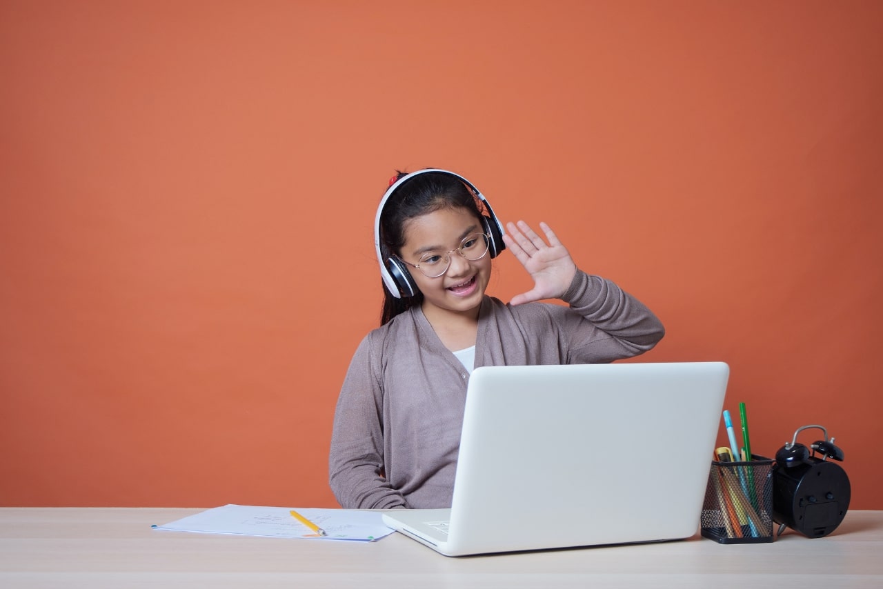 Cute little girl with laptop studying online at home.