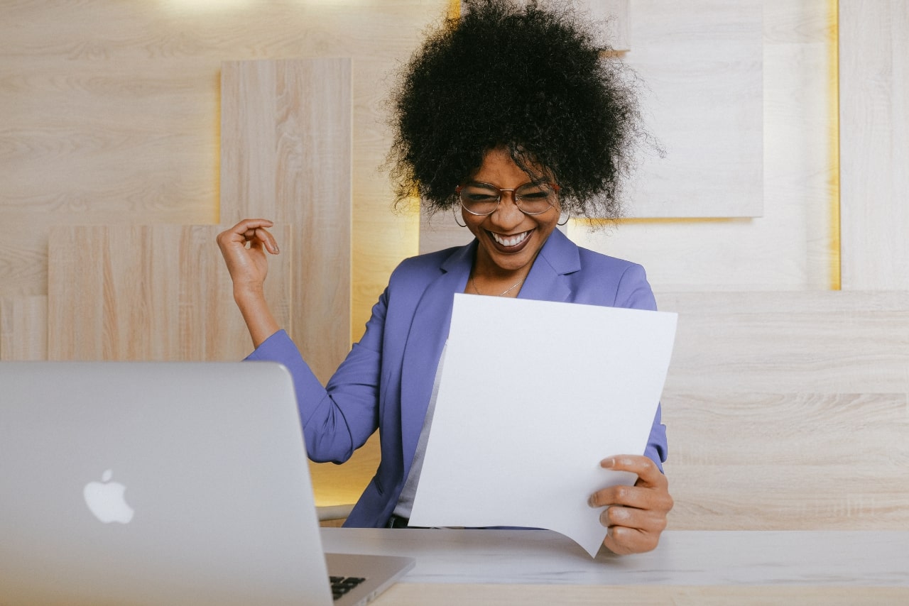Grinning woman holding an online course certificate which she successfuly completed.