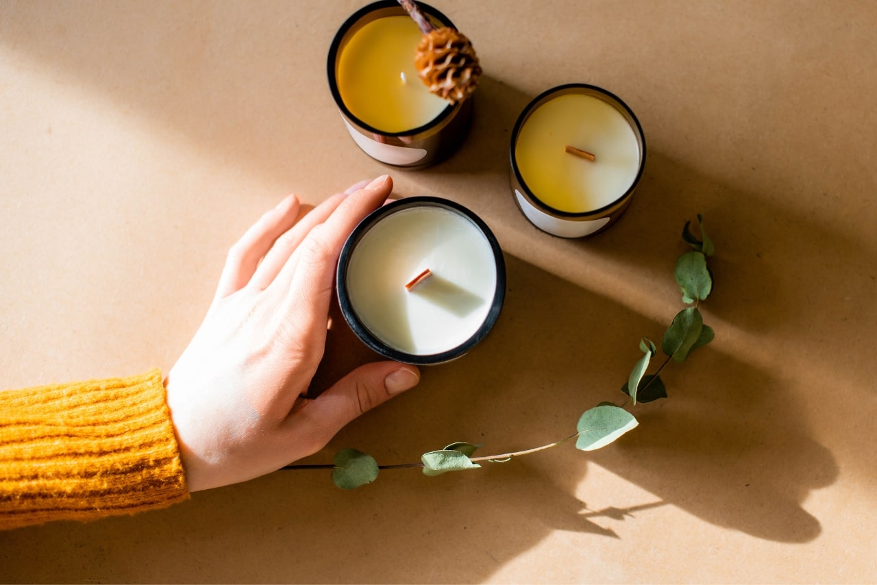 Handmade candle from paraffin and soy wax in glass with leaf on craft background.