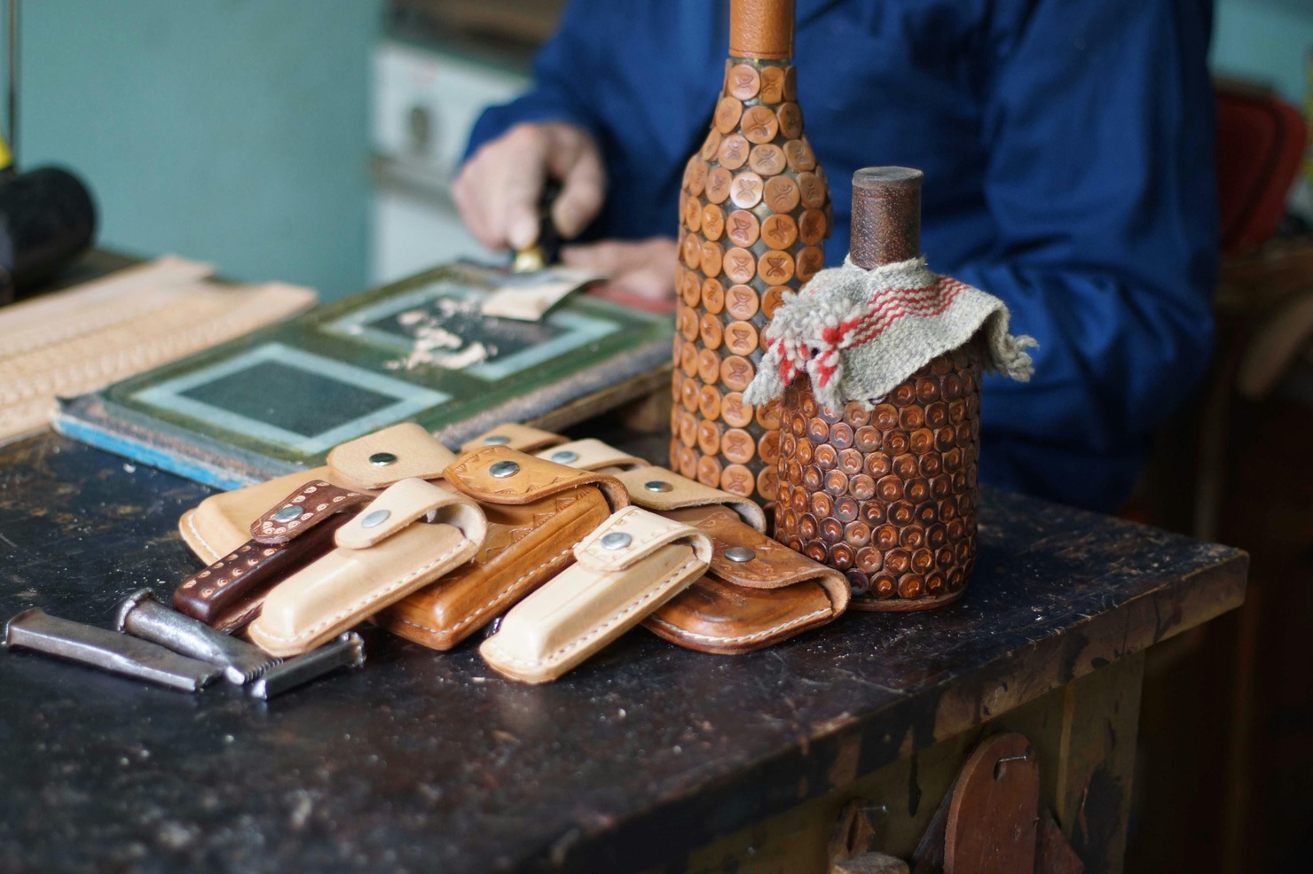 Handmade leather Small Bags and jar holders displayed on table while man is working behind.