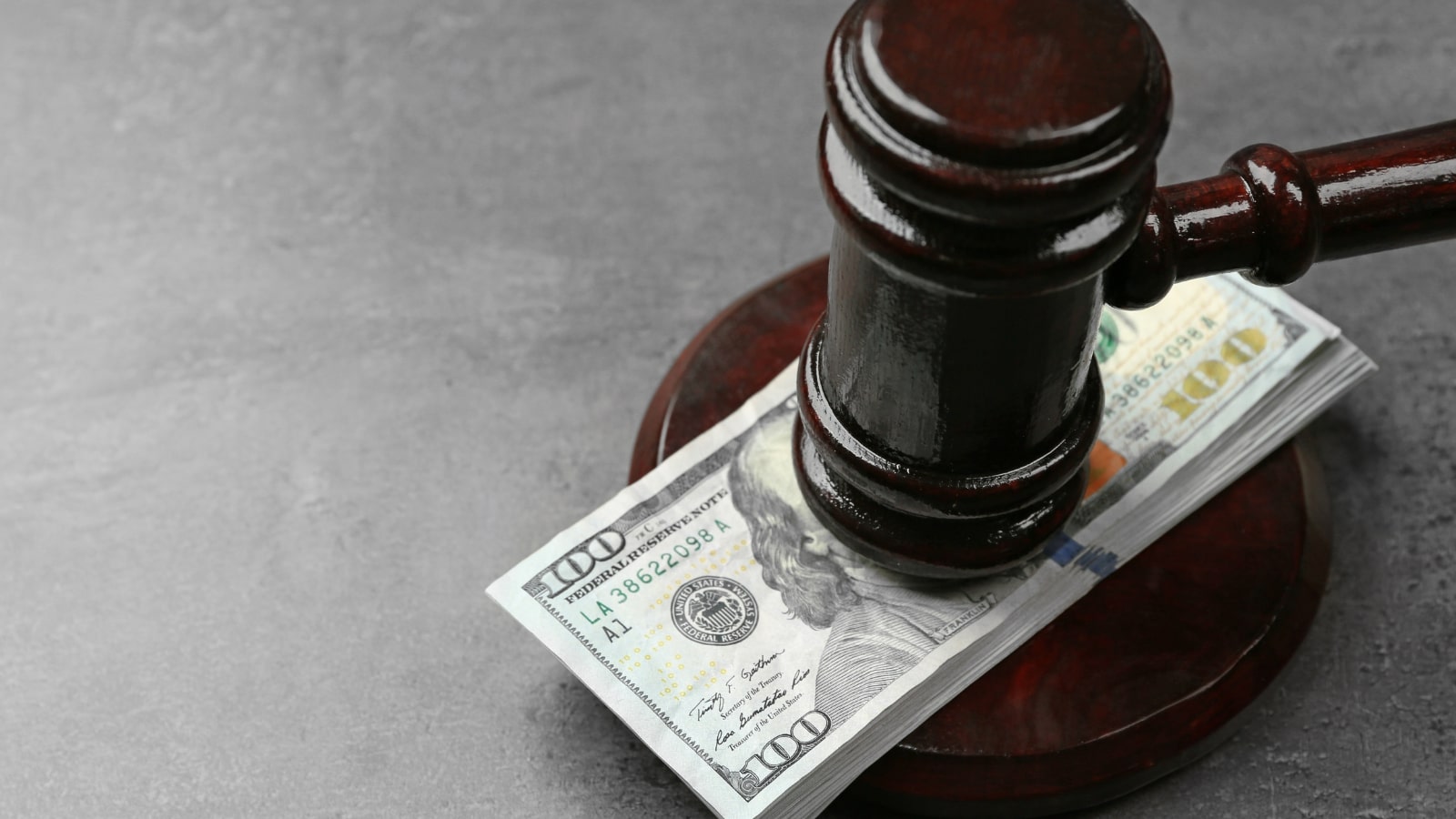 Law gavel with dollars on grey background closeup.