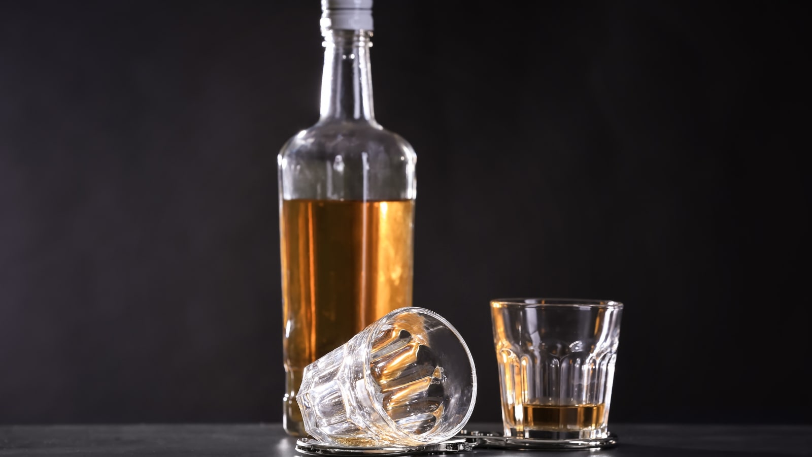 Liquor liability insurance concept bottles of alcohol alongside handcuffs.