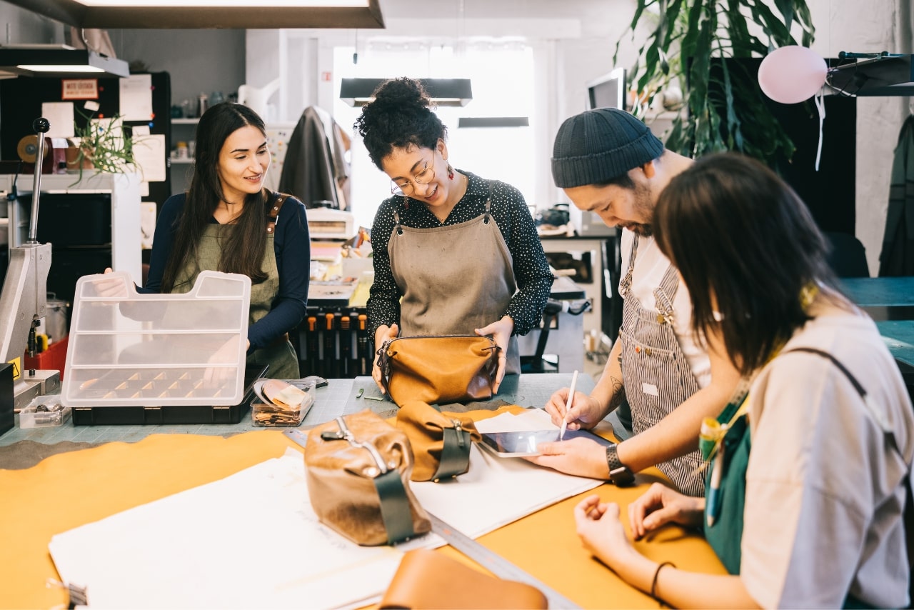 Photo of artisans in a leather workshop studio discussing new product prototype.