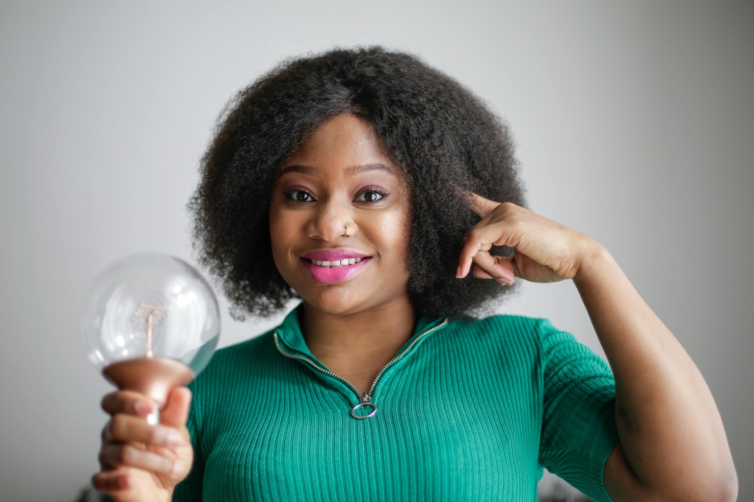 Positive young African American lady holding light bulb in hand on gray background.