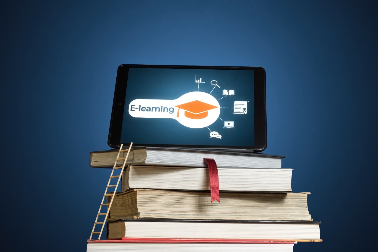 Stack of books with ladder and tablet on the desk.