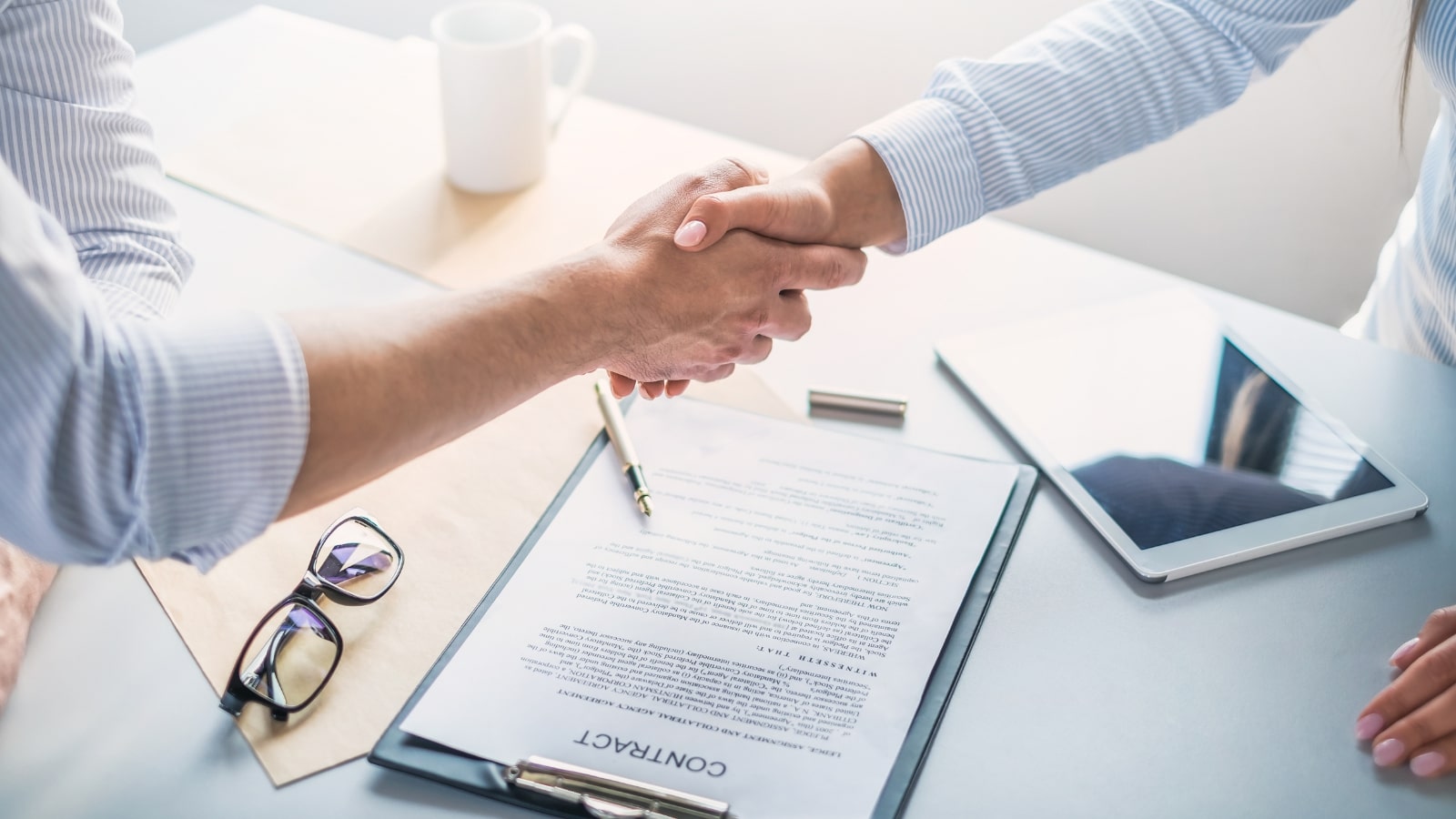 Two people shake hands after signing a contract.