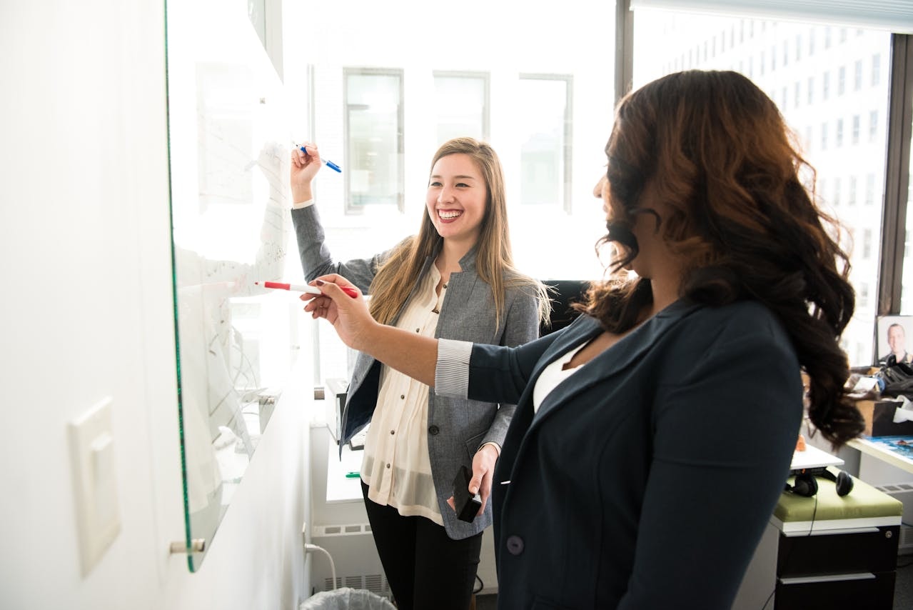 Two women writing and discussing in front of a dry-erase board
