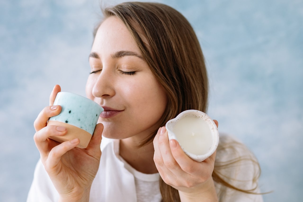 Woman closing eyes while smelling a couple of scented candles.