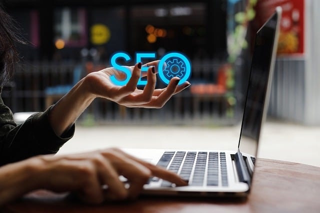 Woman holding the words SEO on one hand while other hand is on her laptop.