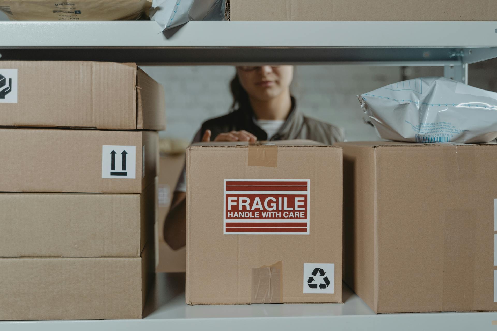 A female warehouse worker is taking a box from the shelf.