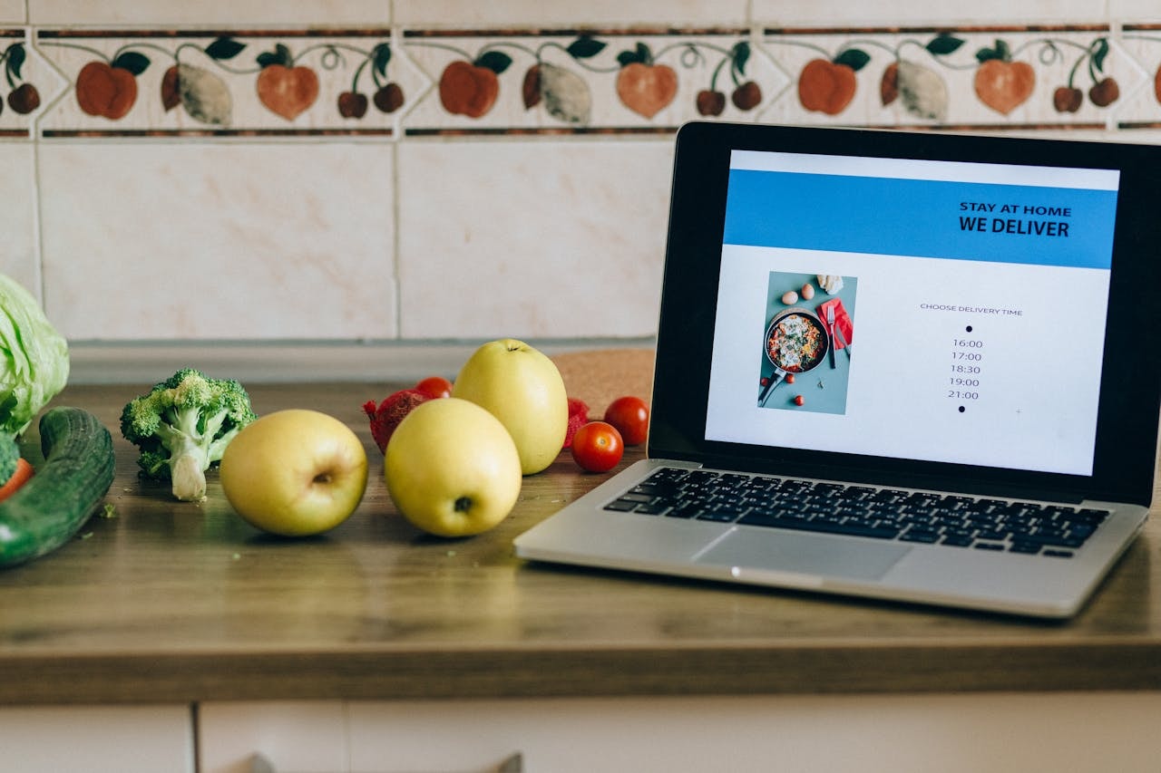 A laptop placed next to vegetables and showing a website of fresh produce