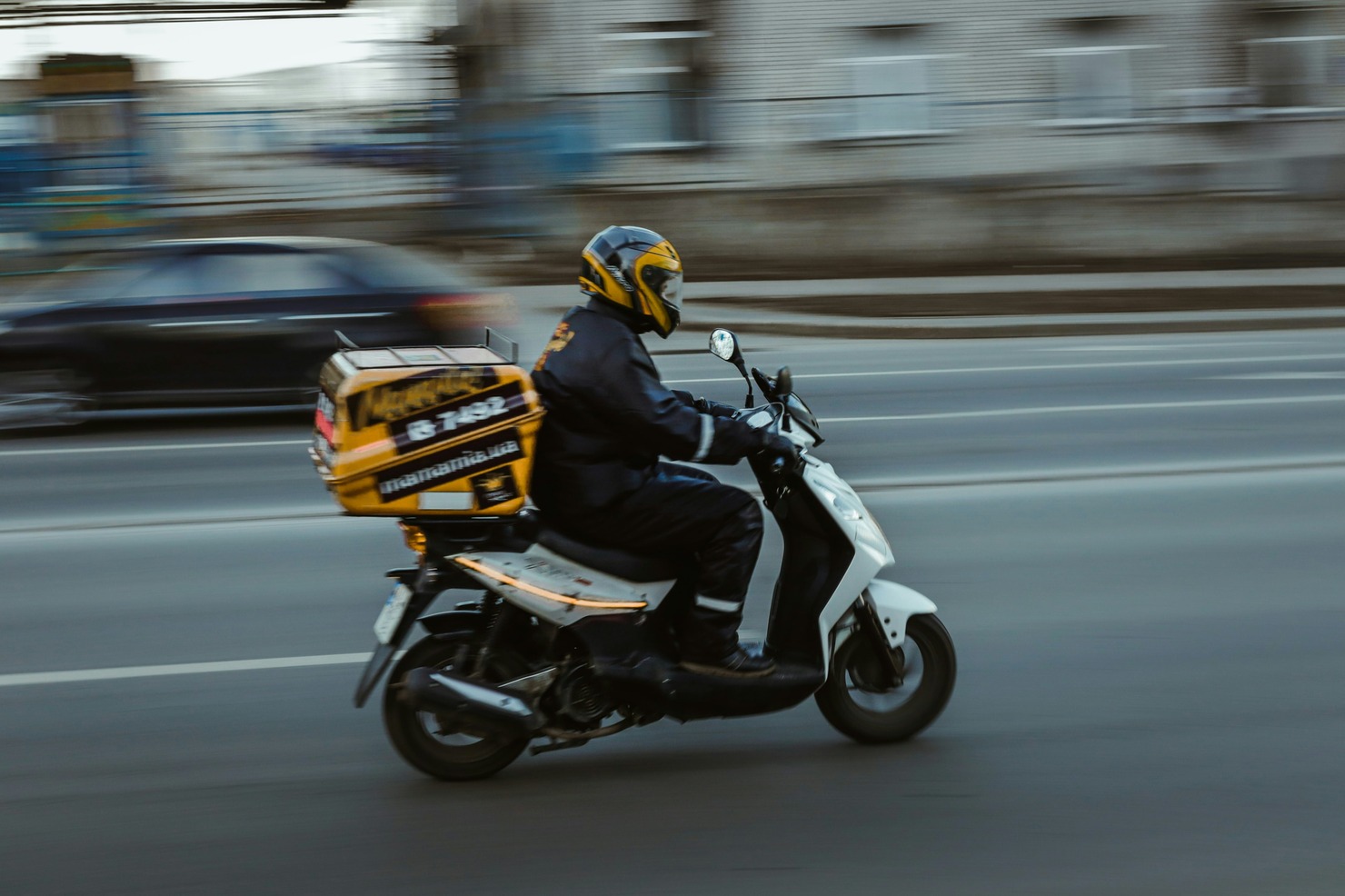 A parcel delivery person is on their way on a scooter.