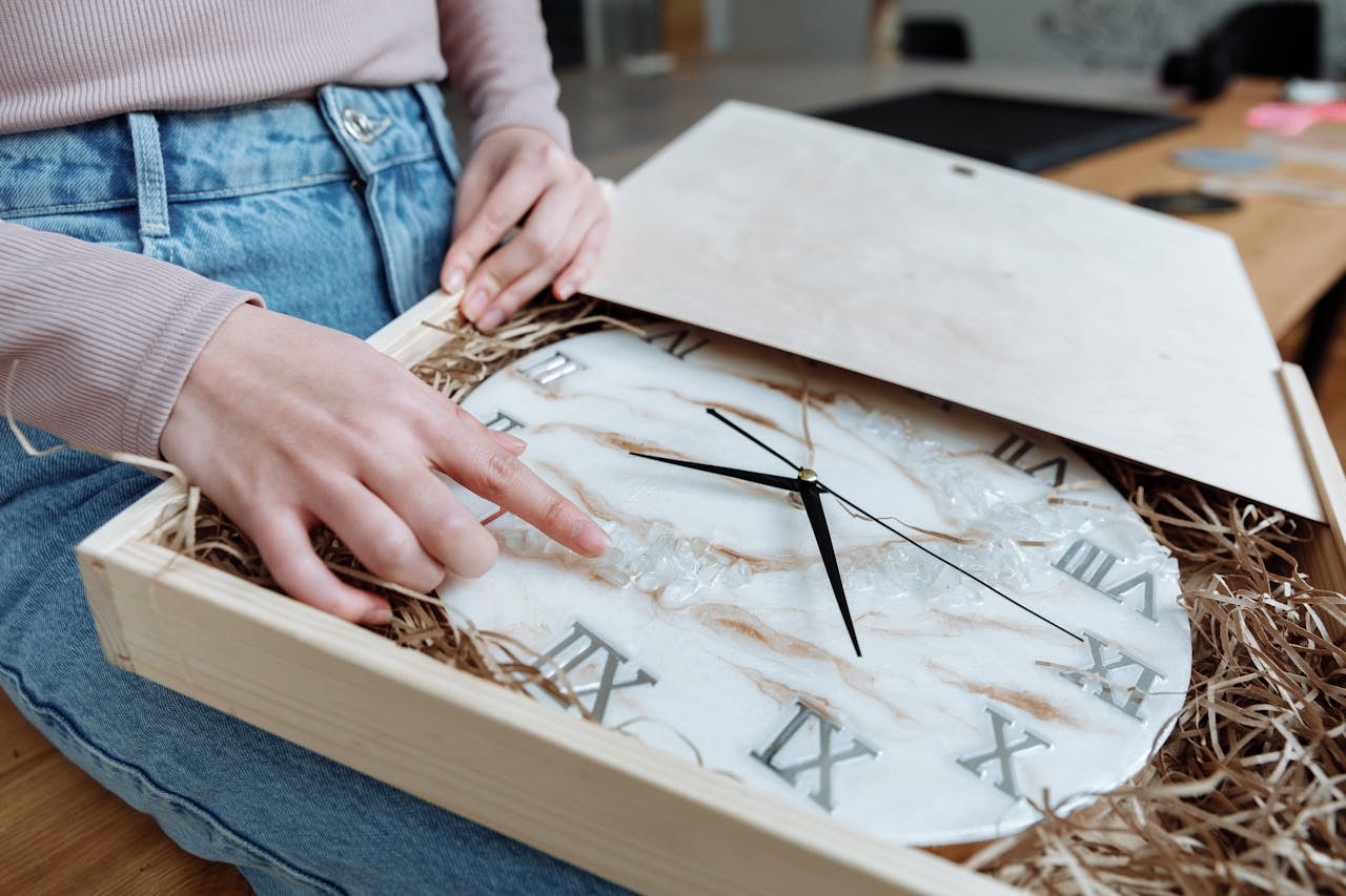 A person packing a wall clock into a wooden box